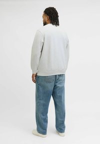 Szara sweatshirt z prążkowanymi mankietami, w połączeniu z luźnymi jasnoniebieskimi dżinsami i białymi sneakersami, widziana z tyłu.