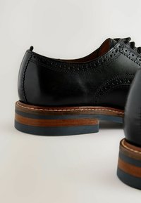 Czarne skórzane buty z wzorem brogue, z podwyższoną drewnianą podeszwą z niebieskimi i brązowymi akcentami oraz gładkim, wypolerowanym wykończeniem.