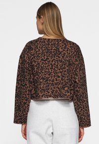 Sweatshirt court avec un imprimé léopard marron et noir. Fabriqué en tissu doux avec des manches longues et un col rond, présentant un ourlet brut.