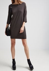 Robe gris charbon avec des manches trois-quarts, une coupe ample et un col rond, assortie à des chaussettes noires mi-mollet et des chaussures à plateforme.