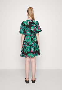 Vestido preto com estampados de folhas verdes e rosas, mangas bufantes, cintura ajustada e bainha com volantes. Usado com sapatos de plataforma pretos.