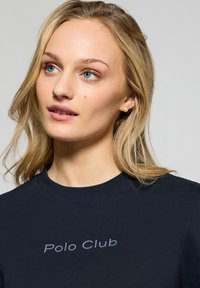 T-shirt bleu marine en tissu doux, présentant un col rond et un logo "Polo Club" en gris clair, positionné centralement sur la poitrine.