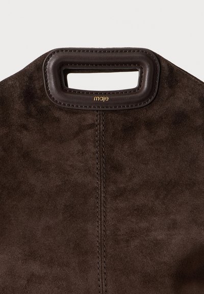 Sac en daim marron foncé avec une poignée découpée rectangulaire bordée de cuir lisse et petit logo doré "maje" sous la poignée.