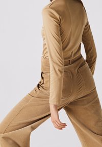 Tan ribbed corduroy pants with a high waist, featuring two back pockets, paired with a lightweight tan long-sleeve top.