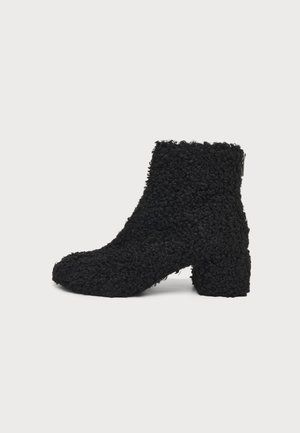 Bottine noire à la cheville en tissu duveteux texturé avec un talon bloc, présentée de profil sur un fond clair uni.