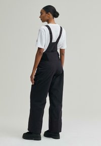 Salopetă neagră cu bretele ajustabile, dotată cu buzunare și o țesătură texturată. Purtați peste o cămașă albă și asortată cu pantofi negri.