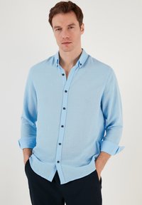 Camicia button-up azzurro chiaro realizzata in un tessuto testurizzato, con colletto, maniche lunghe risvoltate ai polsini e bottoni scuri.