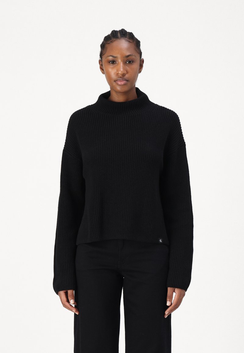Maglione nero a coste con un colletto alto e maniche lunghe, caratterizzato da una vestibilità rilassata e un piccolo logo sul fondo.