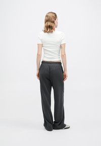 Biała dopasowana koszulka i szare luźne dresy z elastycznym pasem i kieszeniami, widok z tyłu. Gładka tekstura materiału.