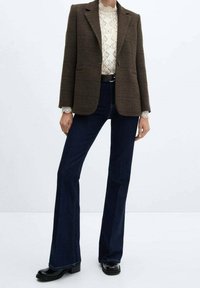 Brun ternet blazer parret med en mønstret bluse, mørkeblå flared jeans og sorte hælede støvler, hvilket skaber et lagdelt, skræddersyet look.