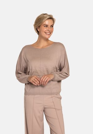 Hellbeiger Pullover mit rundem Ausschnitt, weiten Ärmeln und feiner strukturierter Strickoptik. Kombiniert mit passenden hellbeigen Hosen.
