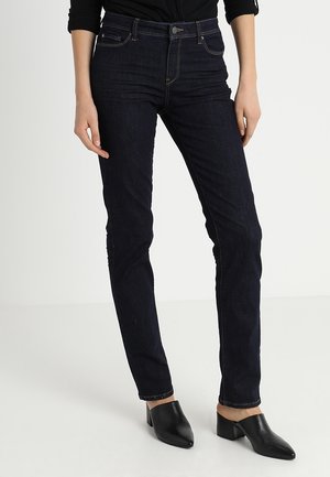Mørkeblå skinny jeans lavet af denim, med fem lommer, bæltestropper og lynlås. Båret med sorte mule-sko.