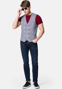 Szary kamizelka w kratę z podwójnym zapięciem, zestawiona z bordowym t-shirtem, przetartymi niebieskimi dżinsami i granatowymi trampkami. Na oczach niebieskie okulary przeciwsłoneczne.