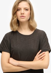 T-shirt noir à manches courtes avec un col rond et des manches retroussées, fabriqué en tissu léger et légèrement texturé.