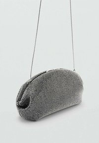 Bolso de mano metálico plateado con forma redondeada, cubierto de pequeños strass y una simple correa de cadena. Textura suave con cierre de pestillo.