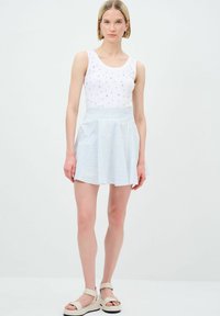 Top senza maniche bianco con decorazioni argentate, abbinato a una gonna plissettata a righe azzurre e bianche. Sandali con suola spessa e cinghie.