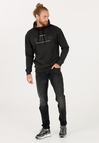 Mörkgrå hoodie med tryck fram, dragsko i huvan och ribbade ärmslut, kombinerad med svarta jeans och grå sneakers med gröna detaljer.