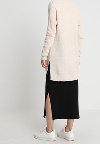Lång, beige texturerad cardigan över en svart midiklänning med sidoslits och vita sneakers. Cardiganen har sänkta axlar och ribbad nederkant.