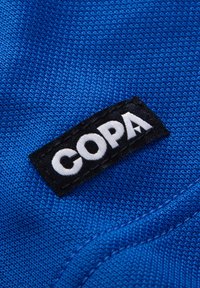 Nahaufnahme eines blau strukturierten Stoffes mit einem schwarzen Etikett, auf dem weißer Text "COPA." steht