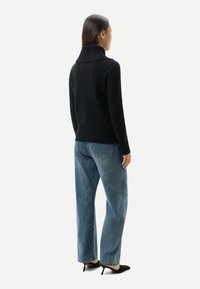 Svart stickad tröja med hög ribbad krage, kombinerad med lösa blå jeans i denim. Enkel design utan synliga mönster eller detaljer.