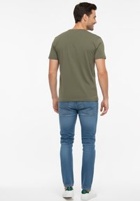 Camiseta de manga corta color verde oliva, cuello redondo, tela suave. Combinada con jeans ajustados azules y zapatos blancos con detalles verdes.