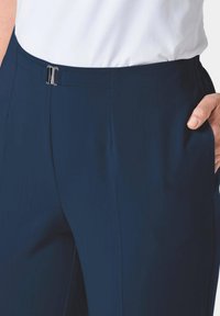 Marineblauwe op maat gemaakte broek met een gladde textuur, voorzien van een metalen haaksluiting en zijzakken. Het ontwerp heeft een aangesloten taille en rechte pijpen.