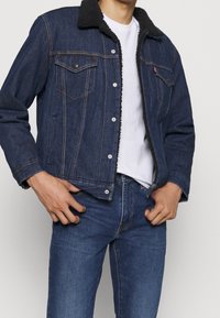 Dark blue denim jacket with a black, fluffy collar, front pockets, and visible stitching details. Paired with matching blue jeans.