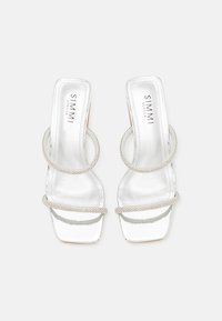 White heeled sandals with a shiny finish, featuring two circular straps embellished with small rhinestones and a square toe design.