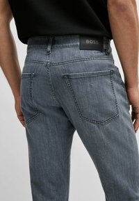 Jeans in denim grigio scuro con un design aderente, dotati di tasche posteriori e di una patch nera con il logo BOSS in vita. Texture liscia.