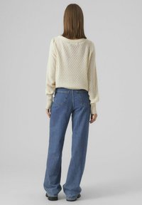 Krämfärgad stickad tröja med en strukturerad mönster, avslappnad passform och ribbade mudd, kombinerad med blå vida denimjeans och svarta platåstövlar.