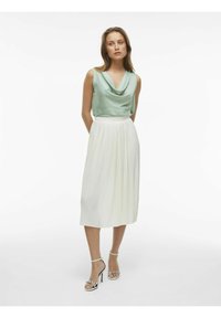 Top s cowl-neck v mentolovozelenkovej saténovej látke skombinovaný s bielou plisovanou midi sukňou. Modelka má na sebe čierne a biele sandále na opätku so strieborným akcentom.