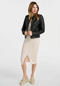 Czarna skórzana kurtka z srebrnymi elementami, dopasowany i skrócony krój. Jasno-beżowa midi sukienka z prążkowanej tkaniny, z rozcięciem z przodu i detalami z guzikami.