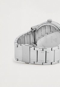 Reloj de acero inoxidable plateado con una banda pulida, que presenta una caja redonda, cierre de broche y un logo grabado en la banda.