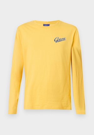 T-shirt jaune à manches longues avec col rond, petit logo "Gant" bleu marine sur le haut de la poitrine à gauche, design uni, présenté sur un fond clair.
