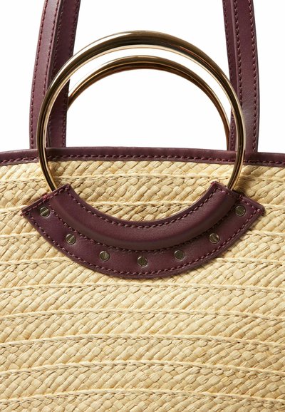 Sac fourre-tout en paille tissée avec des accents en cuir bordeaux profond, doté d'une poignée métallique ronde et de clous décoratifs sur le bord en cuir.