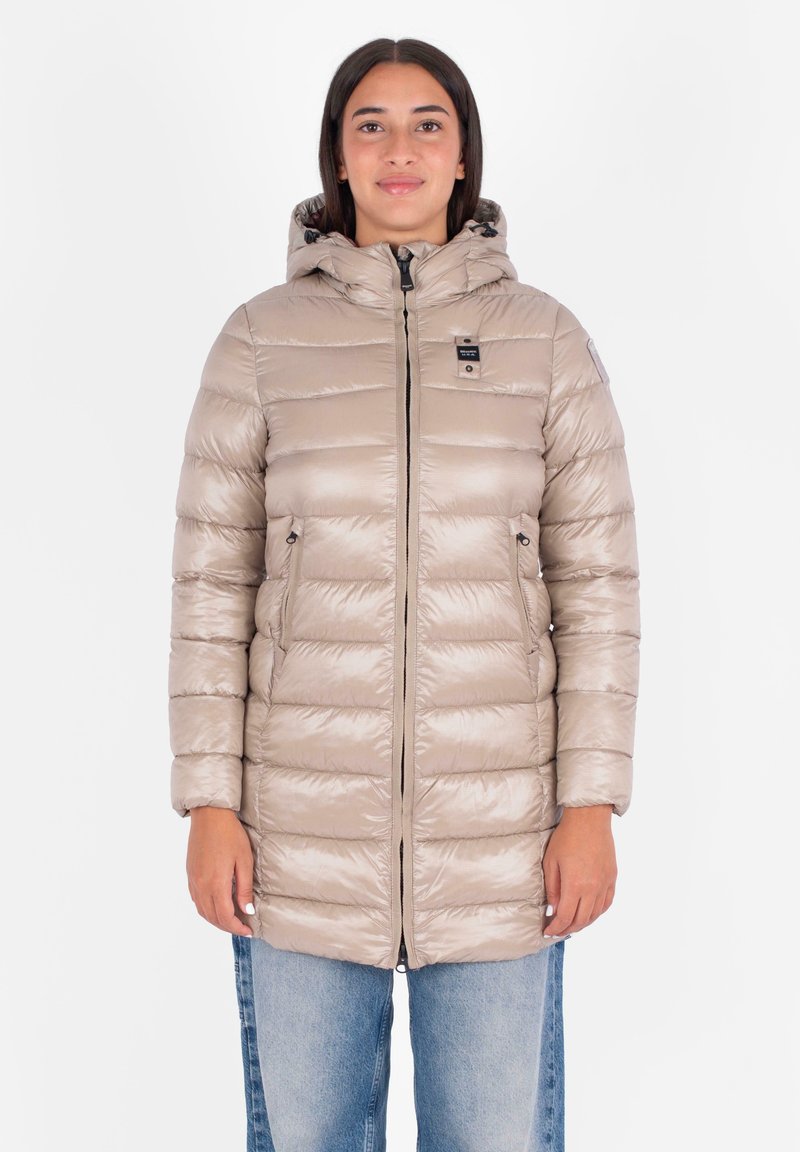 Giacca piumino beige chiaro con cappuccio, design quilted, chiusura con zip, due tasche laterali e una piccola patch con logo sul petto. Texture liscia.
