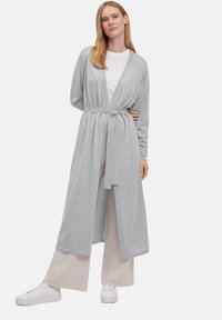 Jasnoszary, długi kardigan z miękkiego materiału, z paskiem w talii, otwartym przodem i długimi rękawami. Połączony z kremowymi spodniami o szerokich nogawkach i białymi trampkami.