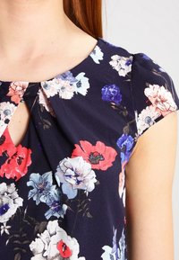 Marinblus med blommor och nyckelhalsring, med röda, rosa och vita blommor. Tillverkad av lätt tyg med en mjuk textur.