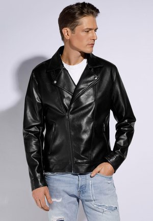 Veste de moto en cuir noir avec un col cranté, fermeture éclair à l'avant et deux poches sur les côtés ; présentée avec un jean déchiré bleu clair.