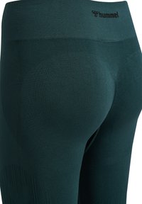 Gros plan sur un legging sans couture vert foncé avec des motifs texturés incurvés et le logo de la marque Hummel sur la ceinture.