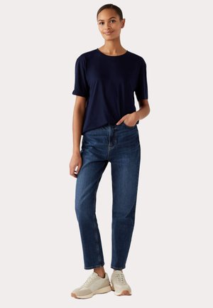 Marineblauw T-shirt met korte mouwen gecombineerd met blauwe spijkerbroeken en beige sneakers. Het T-shirt heeft een ronde hals en een relaxte pasvorm, de spijkerbroeken hebben een rechte snit.