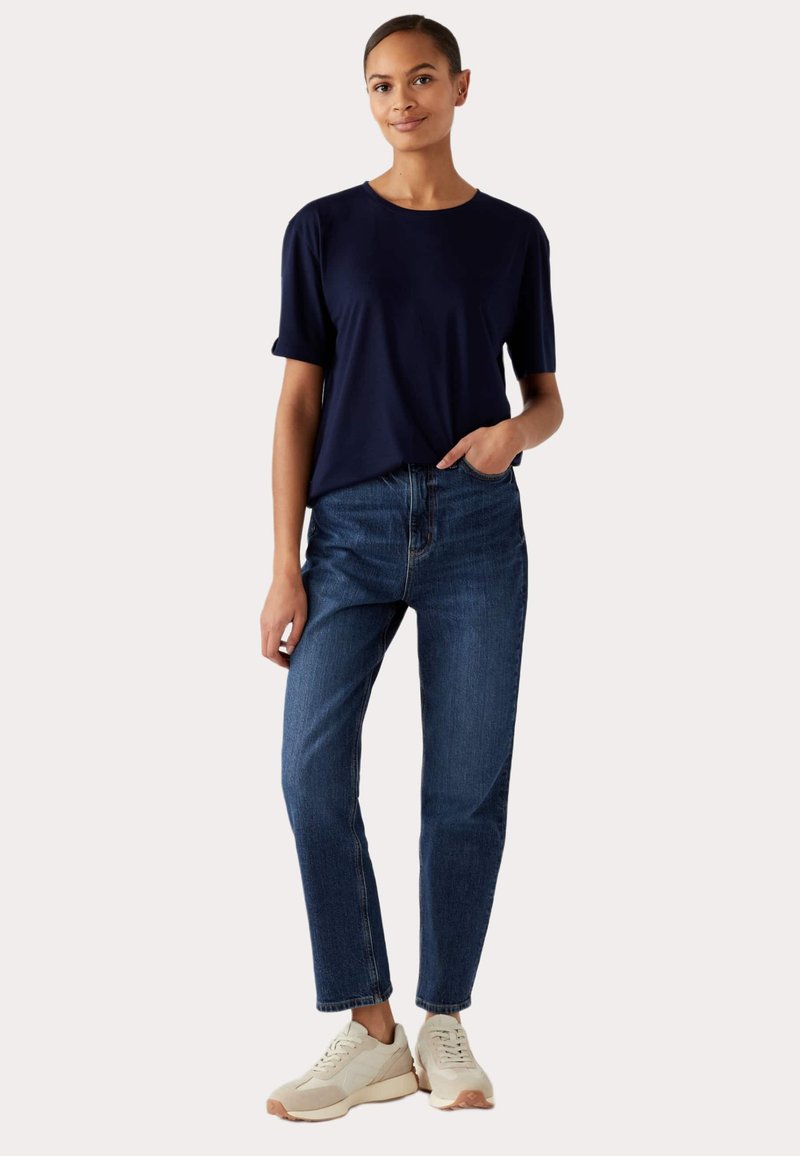 Marineblauw T-shirt met korte mouwen gecombineerd met blauwe spijkerbroeken en beige sneakers. Het T-shirt heeft een ronde hals en een relaxte pasvorm, de spijkerbroeken hebben een rechte snit.