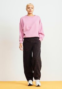 Rosa übergroßer Pullover mit tief sitzenden Schultern, kombiniert mit weiten schwarzen Hosen im Leopardenmuster. Das Model trägt weiße Sneakers. Neutraler Hintergrund.