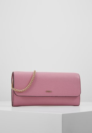 Pochette en cuir rose texturé avec une bandoulière chaîne dorée et un petit logo "Furla" doré sur le devant, posée sur une surface blanche contre un fond uni.