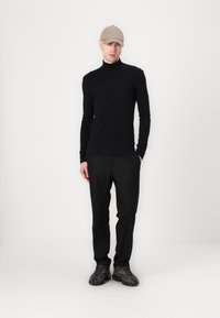 Camiseta de cuello alto negra, ajustada, combinada con pantalones negros de corte ajustado. Una gorra de béisbol beige y zapatillas deportivas oscuras completan el look.