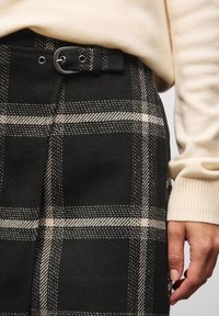 Zwarte en crèmekleurige geruite broek van een gestructureerde wolachtige stof, met een riem met een zilveren gesp en gedetailleerde stiksels.