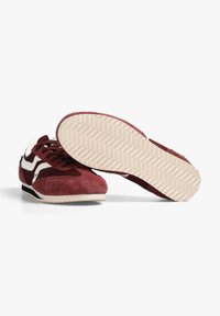 Zapatillas de deporte burdeos con parte superior de ante, acentos blancos y diseño de cordones. Suela de goma texturizada con un patrón de espiga para mayor agarre.