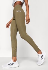 Olivgröna leggings med hög midja och vitt "adidas"-logotyp. Slät textur, figurnära design och sid sömmar för förbättrad passform.