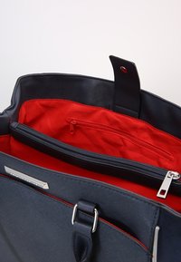 Námořnická taška přes rameno s texturovaným vnějším povrchem, červeným vnitřkem, dvojitými zipovými oddíly a magnetickým uzavíráním. Obsahuje kovové akcenty ve stříbrné barvě.