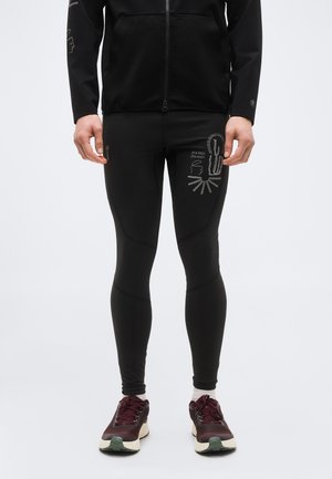 Κολάν με γραφικό κάκτου και ήλιου και κείμενο «Open Roads Open Minds», φορεμένο με μαύρο μπουφάν και μπορντό παπούτσια για τρέξιμο.